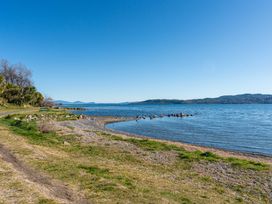 A shoreline along a lake with rocks and a path at Rainbow Point Yacht Club - Taupo Holiday Home Taupo
