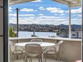 A seating area with a table and chairs overlooking water at Rockstar Retreat - Auckland Holiday Home, Red Beach