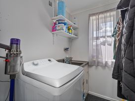 A laundry room with a washing machine and cleaning supplies on the shelf at Endeavour Oasis - Whitianga Holiday Home Whitianga