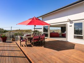 A patio with a dining table and chairs under an umbrella at Ohana - Papamoa Holiday Home, Papamoa