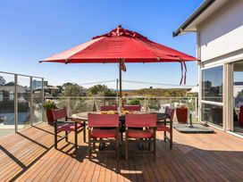 An outdoor dining area with a table and chairs under a red umbrella at Ohana - Papamoa Holiday Home, Papamoa