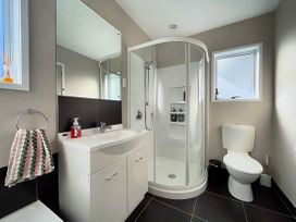 A bathroom with a shower, sink, toilet, and mirror at Vinnie’s haven - Opunake Holiday Home