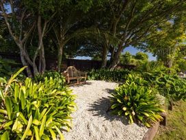 A garden with a bench surrounded by gravel and plants at Poolside on Moffat - Tauranga