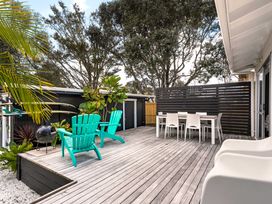 An outdoor deck with chairs and a table at Slice of paradise - Whangamata Holiday Home in Whangamata
