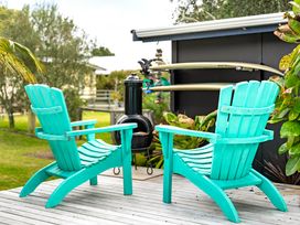 Two turquoise chairs on a wooden deck overlooking a fire pit and surfboards at Slice of paradise - Whangamata Holiday Home in Whangamata