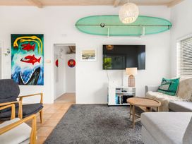 A living room with a surfboard on the wall and a television at Slice of paradise - Whangamata Holiday Home Whangamata