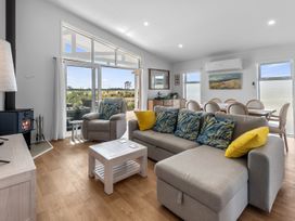 A living room with a sofa, armchairs, and dining area at Pu Corner - Waipu Holiday Home