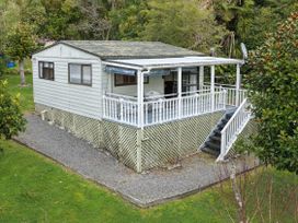 An outdoor view of a cottage with a deck and garden at Treetops & Tide Cottage - Moetapu Holiday Home Moetapu Bay
