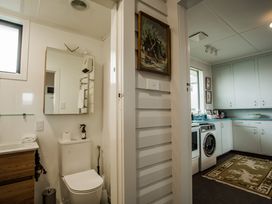 A bathroom with a toilet, sink, mirror, and washing machine at Southern Base - Te Anau Holiday Home, Te Anau