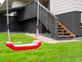 A red swing in the yard with stairs leading to a deck at Surf House - Mangawhai Heads