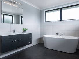 A bathroom with a vanity, sink, mirror and bathtub at Natives Nest - Karikari Peninsula