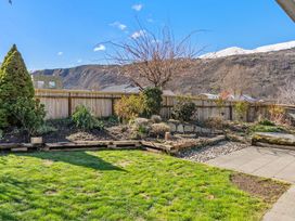 A garden with grass, flower beds, and a pathway at Helmstead Cottage - Arrowtown