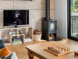 A living room with a TV, wood stove, and chess set at The Cove Escape - Cooks Beach Holiday Home