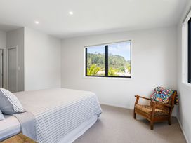 A bedroom with a bed and a chair at The Cove Escape - Cooks Beach