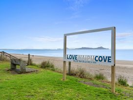 A beach with a sign reading Love Waipu Cove and a bench at Over the Paddock - Waipu Holiday Home in Waipu