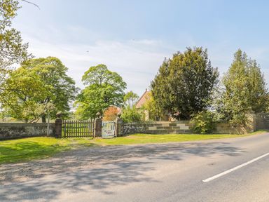 A gated entrance with stone pillars and a wooden fence surrounded by trees next to a road at Fenwick Retreat at Fenwick Lodge in Fenwick near Ponteland