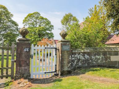 A white wooden gate between stone pillars opening to a garden with trees at Fenwick Retreat at Fenwick Lodge in Fenwick near Ponteland