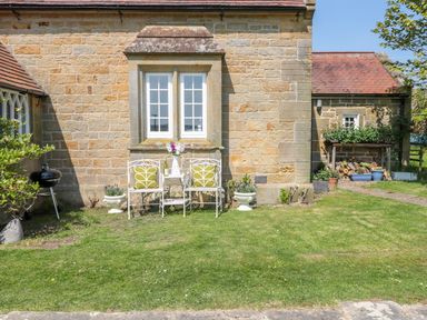 A garden with white metal chairs and a table with flowers against a stone house wall at Fenwick Retreat at Fenwick near Ponteland