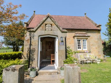 Stone cottage entrance with tiled floor and wooden door with outdoor chairs and table on grass at Fenwick Retreat at Fenwick near Ponteland