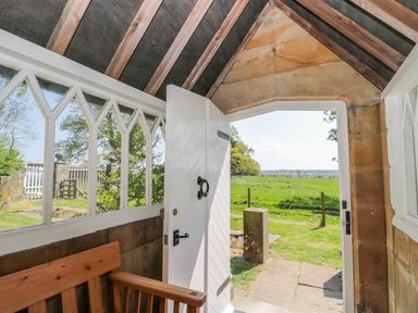 A porch with wooden bench and white door open to a grassy field at Fenwick Retreat at Fenwick Lodge in Fenwick near Ponteland