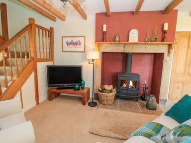 A living room with a wood burning stove fireplace a television on a wooden stand and a staircase with wooden railings at Fenwick Retreat at Fenwick near Ponteland