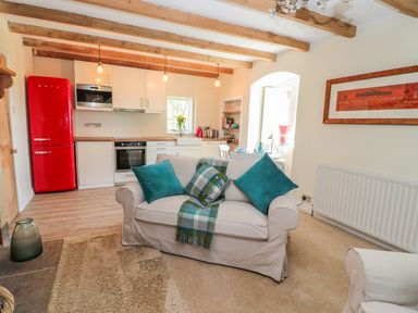 A living room with a beige sofa with teal cushions and a plaid throw blanket near a kitchen with a red fridge and white cabinets at Fenwick Retreat at Fenwick Lodge Fenwick near Ponteland