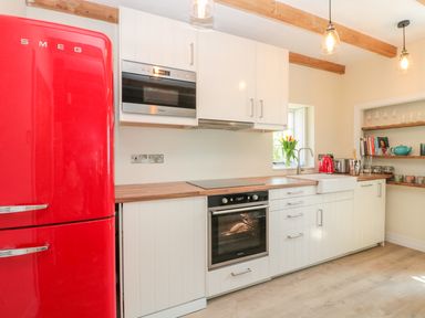 A kitchen with a red refrigerator white cabinets wooden countertops oven microwave and open shelves with cups and books at Fenwick Retreat at Fenwick Lodge in Fenwick near Ponteland