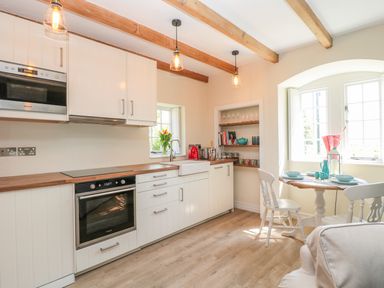 A kitchen with white cabinets a wooden countertop a round dining table with chairs and shelves with kitchenware at Fenwick Retreat at Fenwick near Ponteland