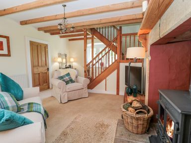 A living room with sofas, a wood stove, a basket of firewood, a staircase, a television, and a wooden door at Fenwick Retreat at Fenwick Lodge in Fenwick near Ponteland