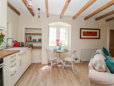 A kitchen and dining area with wooden beams on the ceiling a round table with two white chairs and a sofa with green cushions at Fenwick Retreat at Fenwick near Ponteland