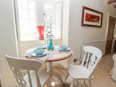 A small wooden dining table with two white chairs set with blue dishware by a window with a red lamp and a framed picture on the wall at Fenwick Retreat at Fenwick Lodge in Fenwick near Ponteland