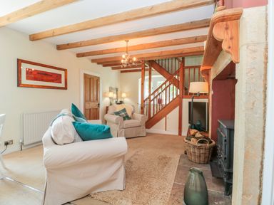 A living room with beige sofas and teal cushions wooden staircase and a fireplace with basket of logs at Fenwick Retreat at Fenwick Lodge in Fenwick near Ponteland