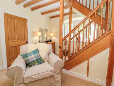 A beige armchair with a plaid cushion and a sheepskin throw next to a wooden staircase and a wooden door at Fenwick Retreat at Fenwick Lodge in Fenwick near Ponteland