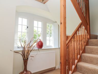 A stairway with wooden railing next to a window with a red vase on the sill and a decorative floor vase with dried branches at Fenwick Retreat at Fenwick near Ponteland