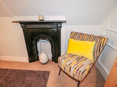 A small black fireplace with a white vase inside and a striped chair with a yellow cushion next to it at Fenwick Retreat at Fenwick Lodge in Fenwick near Ponteland