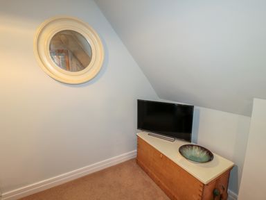 A corner with a wooden chest topped by a television and a decorative bowl with a round wall mirror above at Fenwick Retreat at Fenwick Lodge in Fenwick near Ponteland
