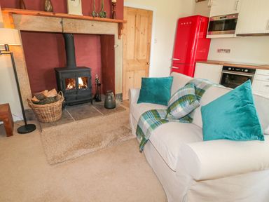 A living area with a fireplace a wood-burning stove a basket of firewood a beige sofa with blue cushions and a kitchen area with red fridge at Fenwick Retreat at Fenwick Lodge in Fenwick near Ponteland