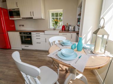 A kitchen with white cabinets red refrigerator wooden round table with blue dishes and white chairs at Fenwick Retreat at Fenwick Lodge in Fenwick near Ponteland