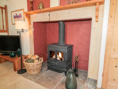 A living room with a wood burning stove in a stone fireplace with a basket of logs and TV on a wooden stand at Fenwick Retreat at Fenwick near Ponteland