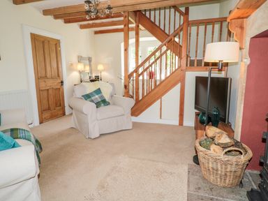 A living room with armchairs a wooden staircase and a basket of firewood at Fenwick Retreat at Fenwick Lodge in Fenwick near Ponteland