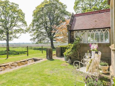A garden area with two white metal chairs and a small table with drinks and flowers outside a stone building with leaded windows at Fenwick Retreat at Fenwick Lodge in Fenwick near Ponteland