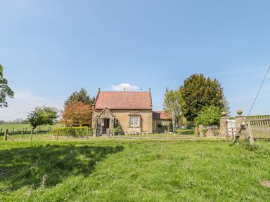 A stone house with a red tiled roof surrounded by trees and a grassy field at Fenwick Retreat at Fenwick Lodge in Fenwick near Ponteland