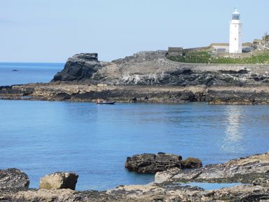 A rocky coastline with a white lighthouse and a small boat on the water at Trevow in Camborne