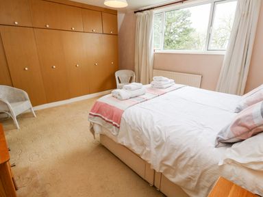 A bedroom with a double bed towels on the bed two wicker chairs and wooden wardrobes at Trevow in Camborne