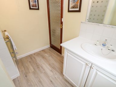 A bathroom with a white sink and cabinet wooden door with frosted glass and towel rack on laminate floor at Trevow in Camborne