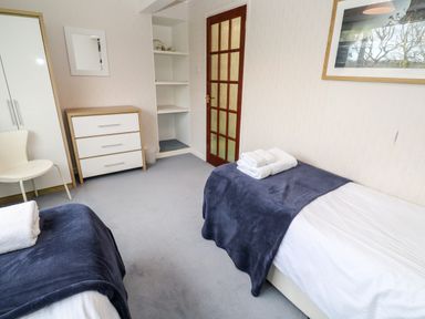 A bedroom with two single beds with towels on them a chest of drawers a white chair a wardrobe and a framed picture at Trevow in Camborne