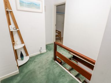 A hallway with green carpet and wooden railing next to a staircase and a shelf with decorative items at Trevow Camborne