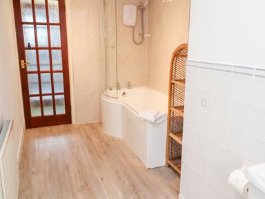 A bathroom with a wooden door a bathtub with a shower a wicker shelf and a radiator at Trevow Camborne