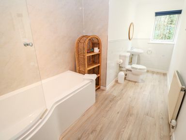 A bathroom with a bathtub toilet sink wicker shelf and a window at Trevow in Camborne