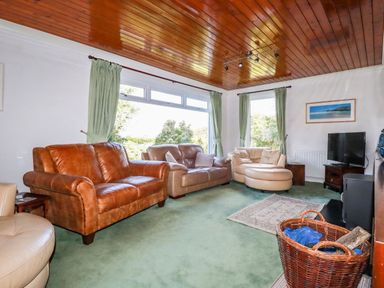 A living room with leather sofas a television on a stand and a basket with firewood at Trevow in Camborne
